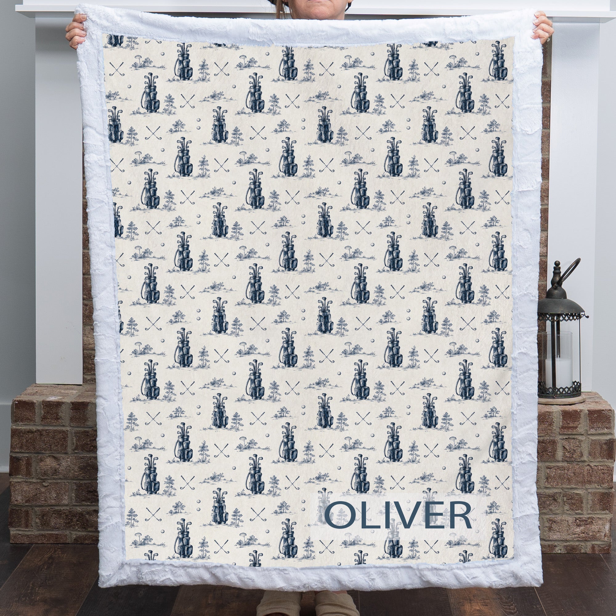 Woman holding personalized golf-print minky blanket with name Oliver, white trim, by fireplace