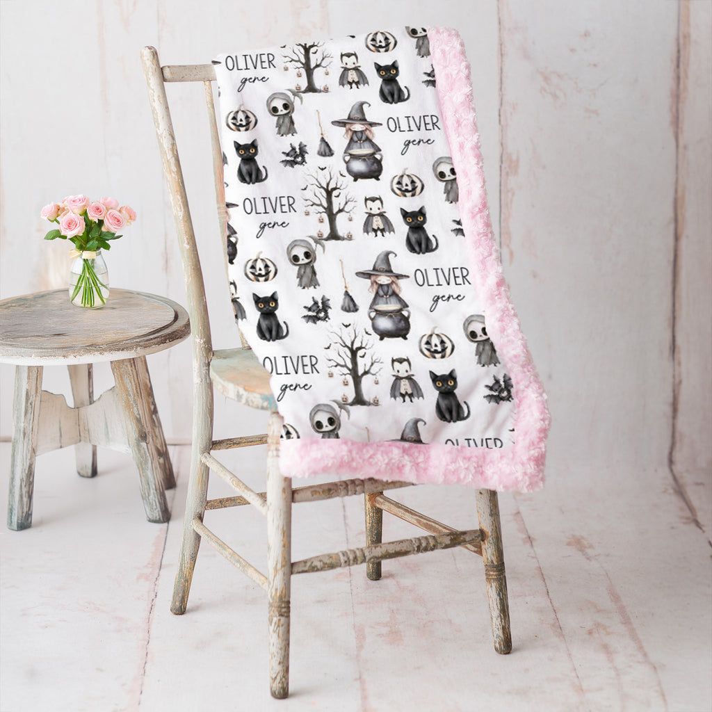 Personalized Halloween minky blanket with pink faux fur trim draped over vintage chair beside pink roses