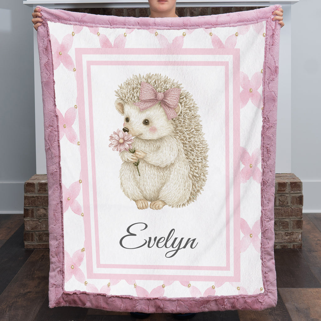 Personalized Luxe Cuddle Minky hedgehog baby blanket held up fully open showing Evelyn name and pink border