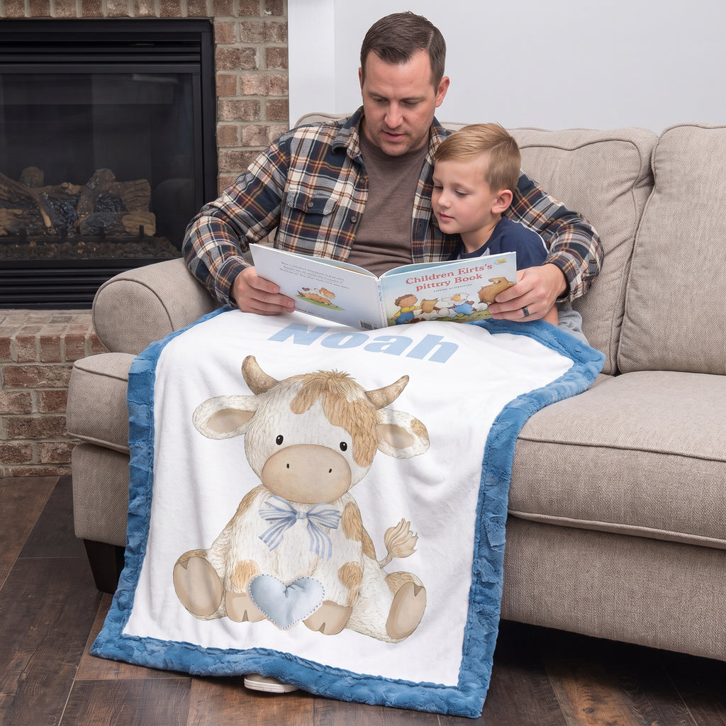 Personalized Highland cow minky baby blanket with Noah's name, draped on couch as dad reads to son