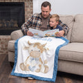 Personalized Highland cow minky baby blanket with Noah's name, draped on couch as dad reads to son
