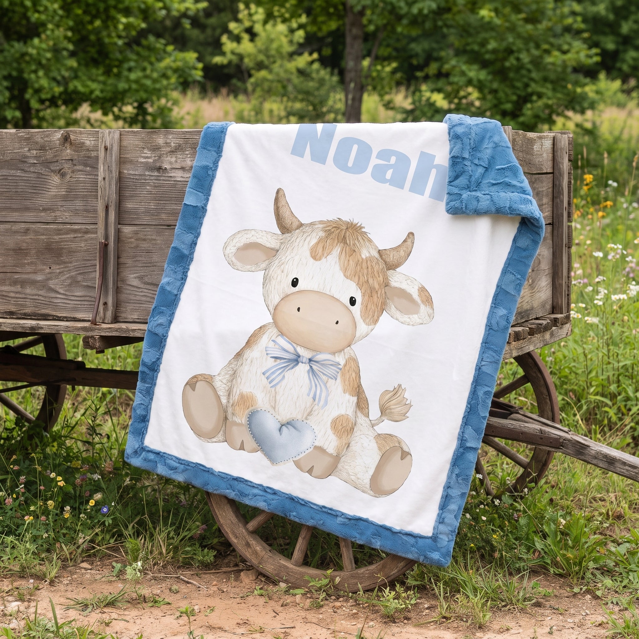 Personalized Highland cow minky baby blanket with Noah's name draped on rustic wagon wheel outdoors