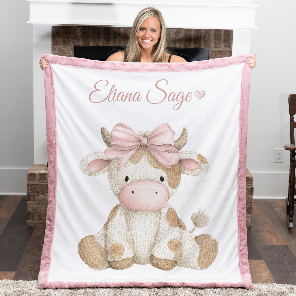 Woman holding personalized highland cow minky blanket with pink trim near fireplace