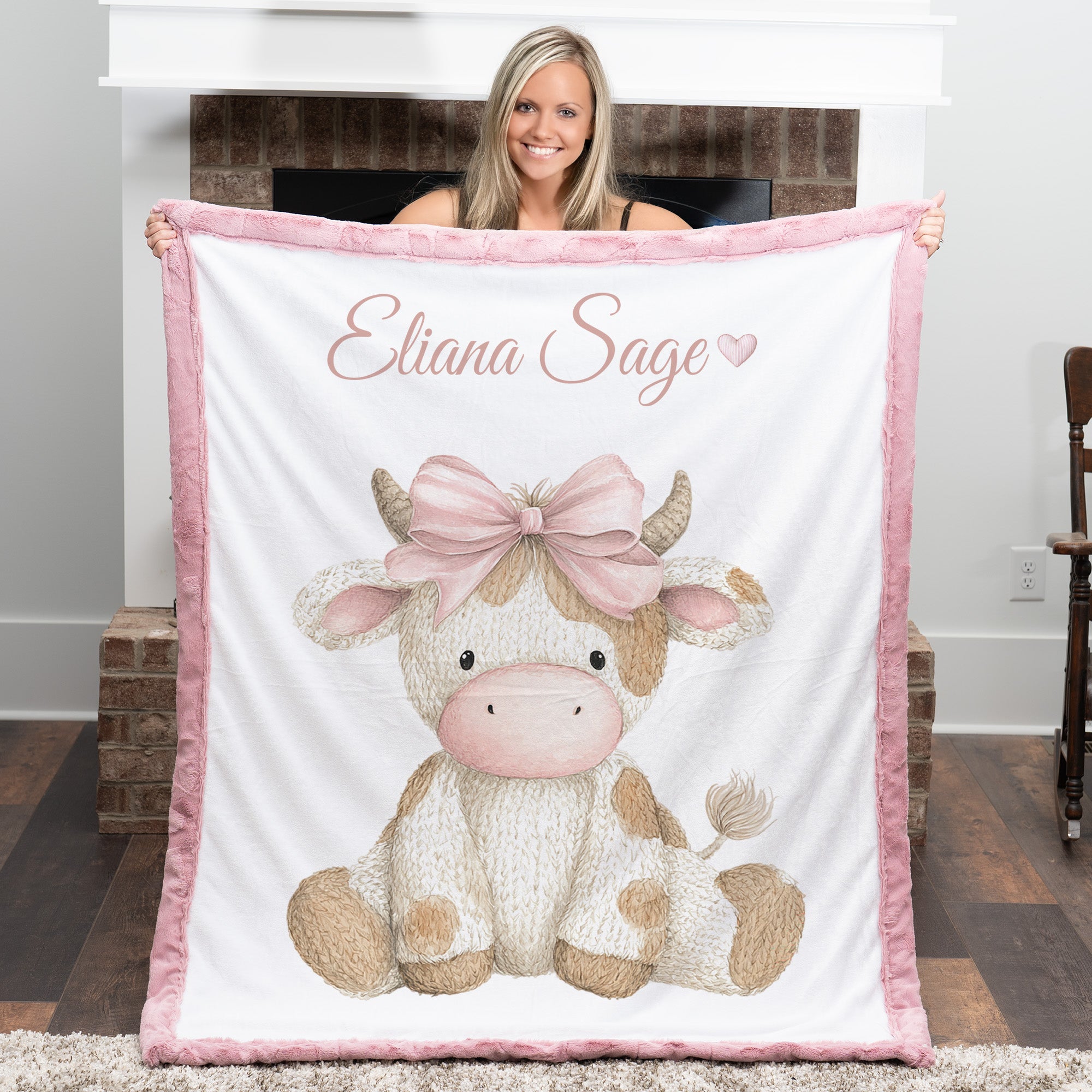 Woman holding personalized highland cow minky blanket with pink trim near fireplace