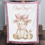 Woman holding personalized highland cow minky blanket with pink trim over fireplace mantel