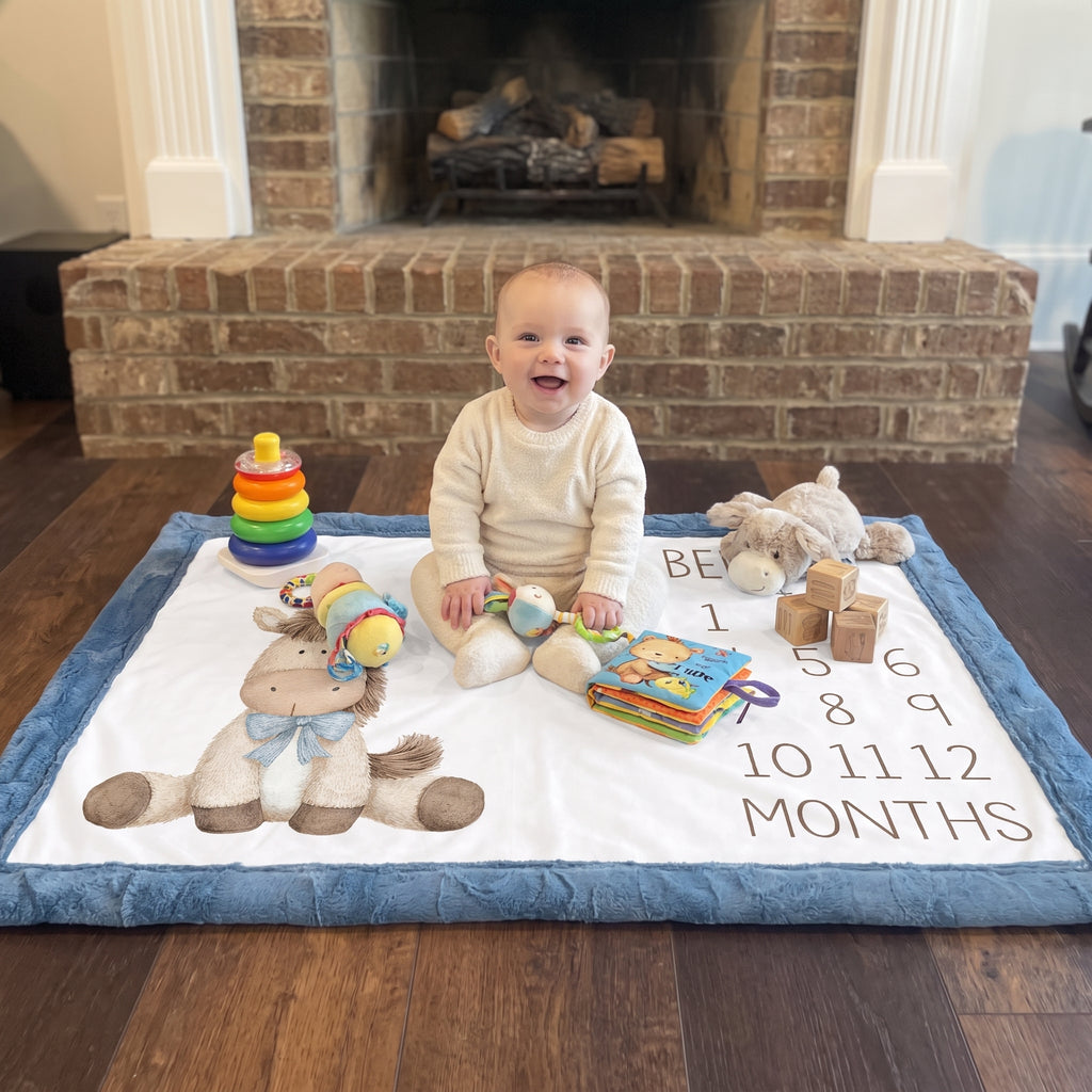 Baby sitting on personalized horse milestone blanket with toys by fireplace