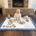 Baby sitting on personalized horse milestone blanket with toys by fireplace