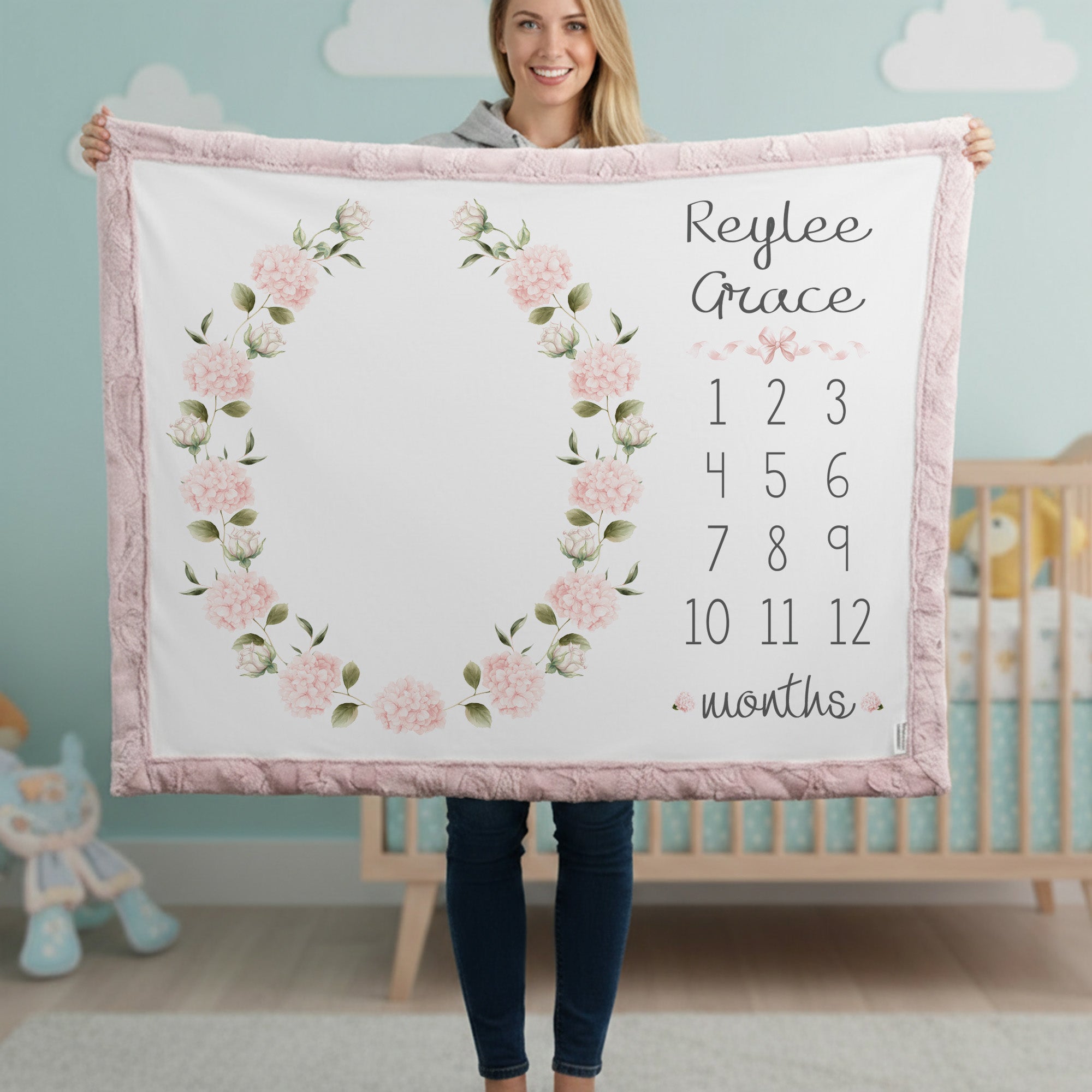 Woman holding personalized hydrangea milestone minky blanket with pink trim in cloud nursery
