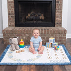 Baby sitting on personalized hydrangea wreath milestone blanket with toys by fireplace