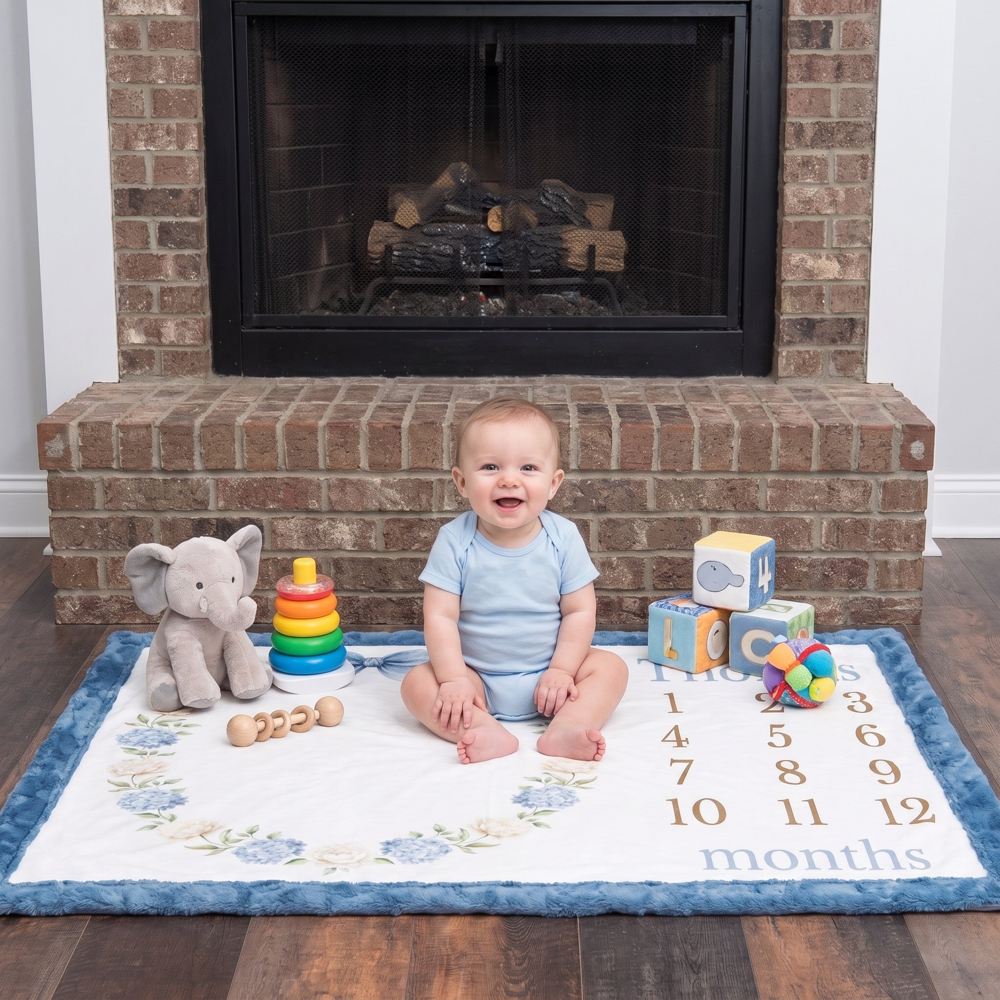 Baby sitting on personalized hydrangea wreath milestone blanket with toys by fireplace