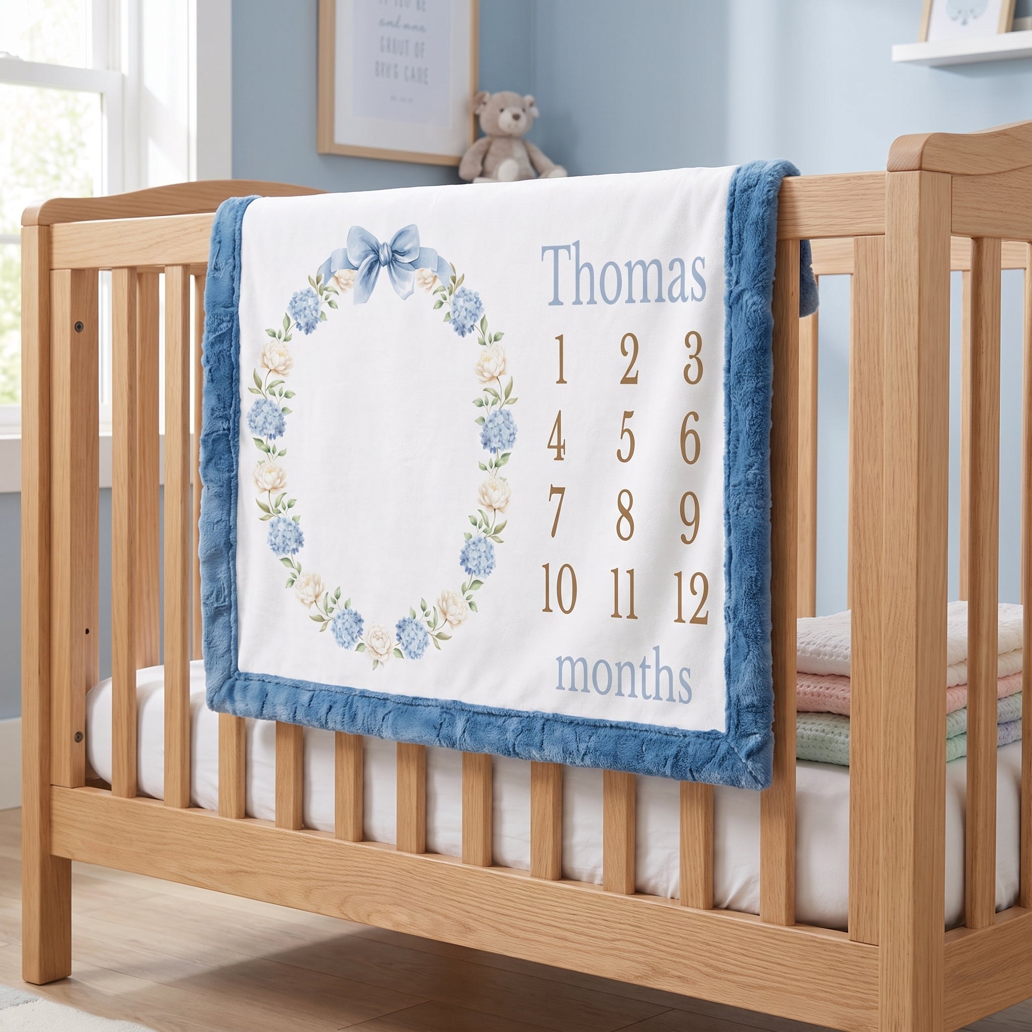 Personalized milestone minky blanket with hydrangea wreath draped over crib in nursery