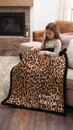 Girl sitting on couch with personalized leopard print minky blanket, black trim, by fireplace