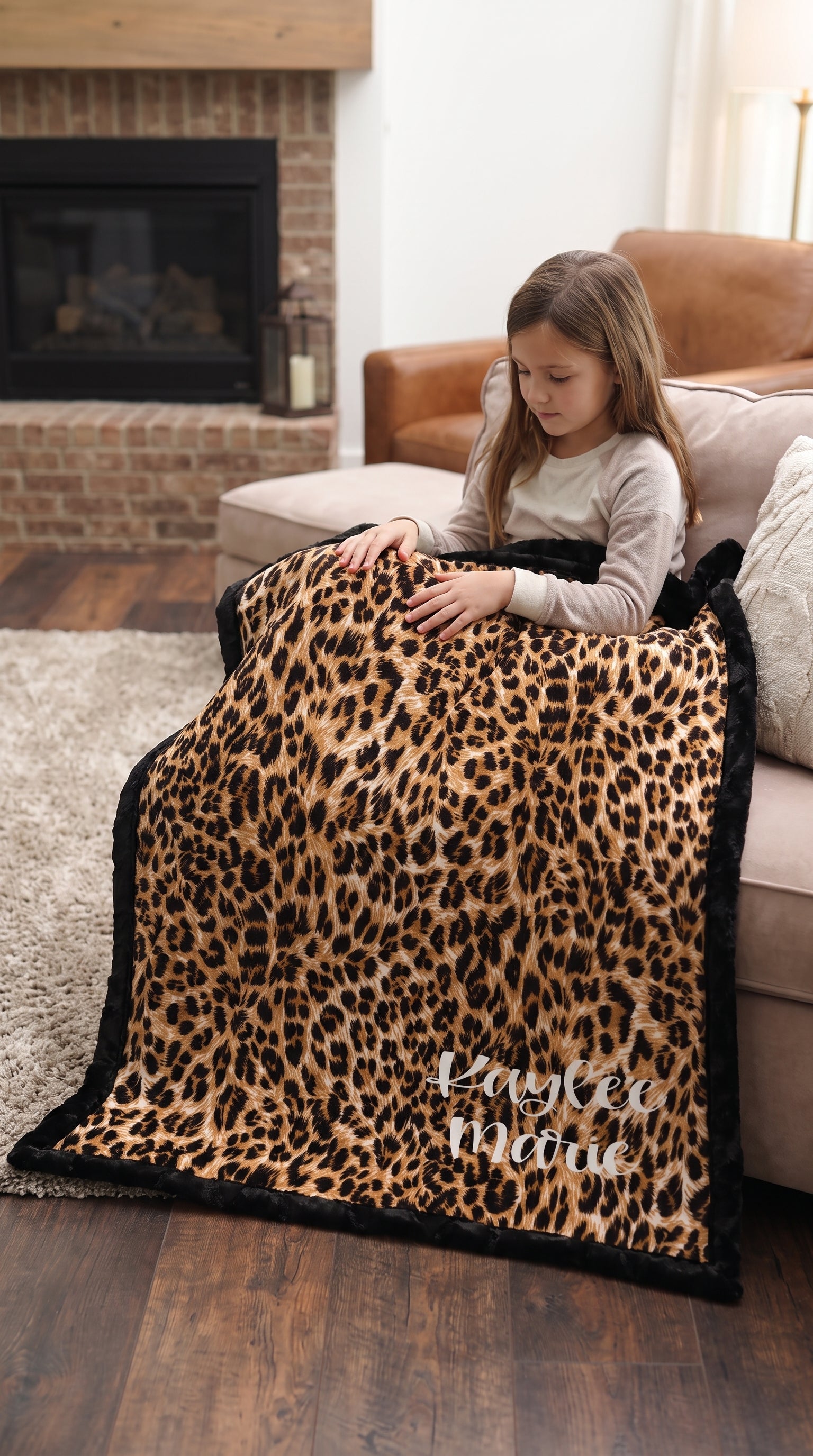 Girl sitting on couch with personalized leopard print minky blanket, black trim, by fireplace