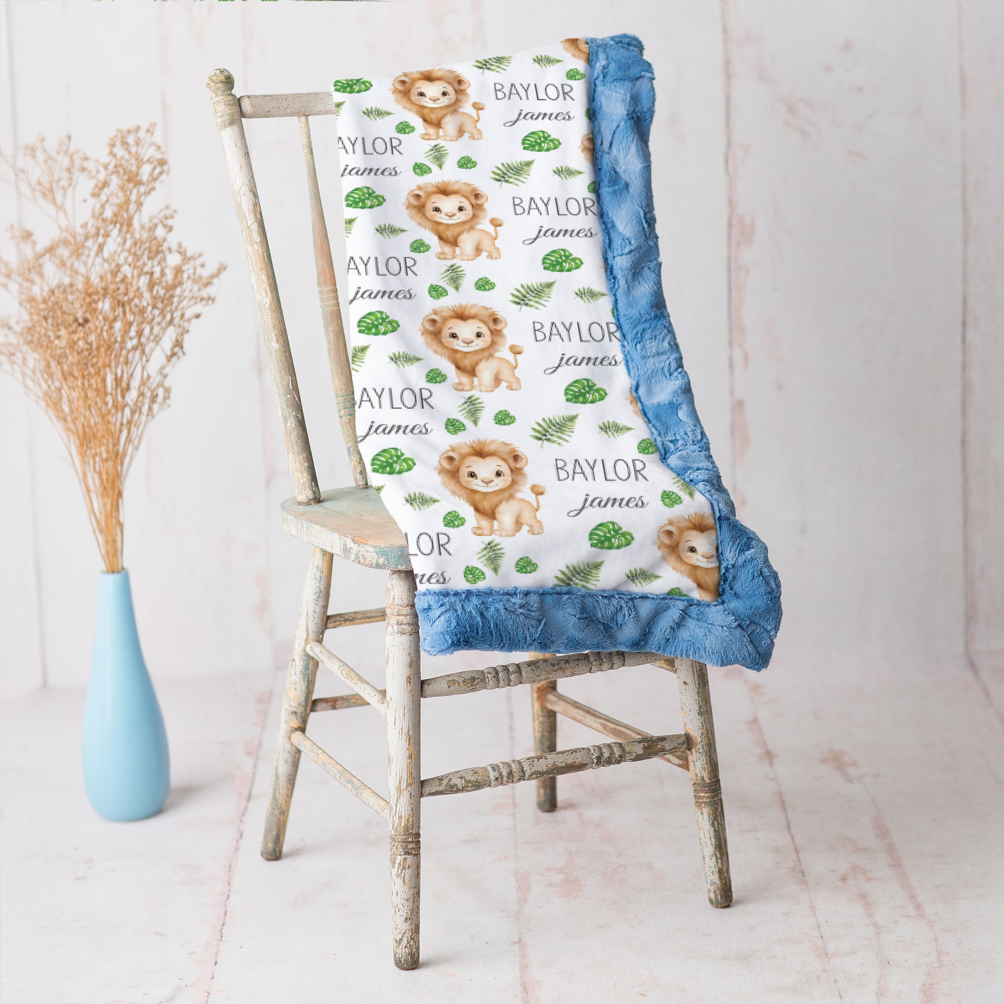 Lion print baby blanket with blue minky trim draped over vintage rustic chair