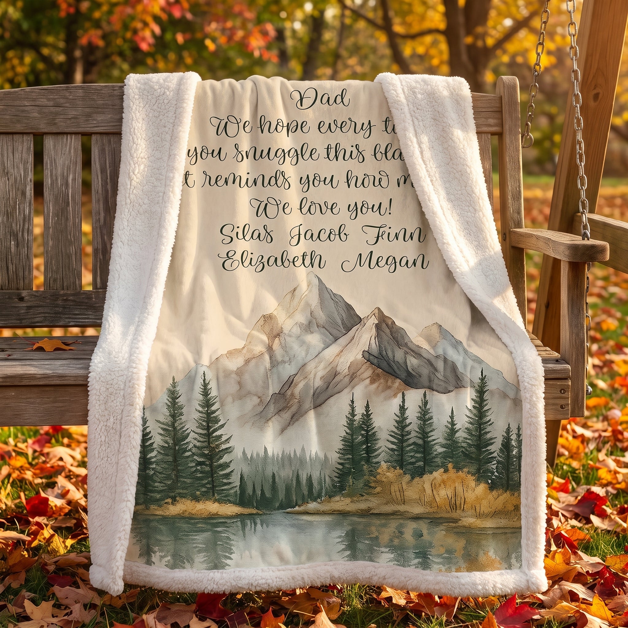 Personalized mountain lake blanket with a Dad message draped over a wooden bench amid autumn leaves