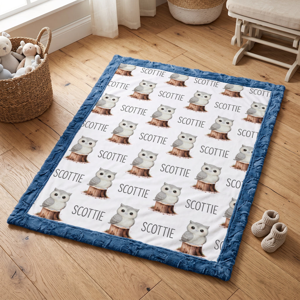 Personalized owl minky blanket with blue trim folded flat lay on wood floor
