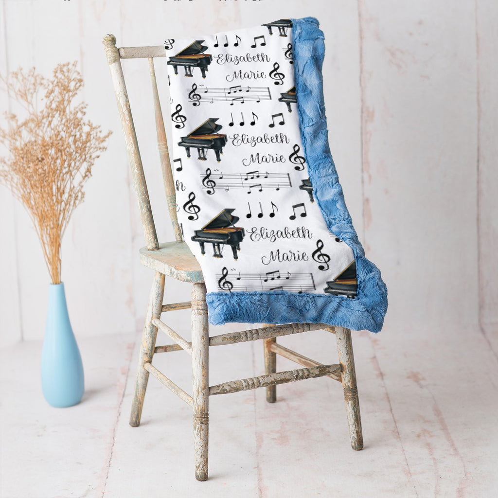 Personalized piano minky blanket with blue trim draped over vintage chair beside dried flowers