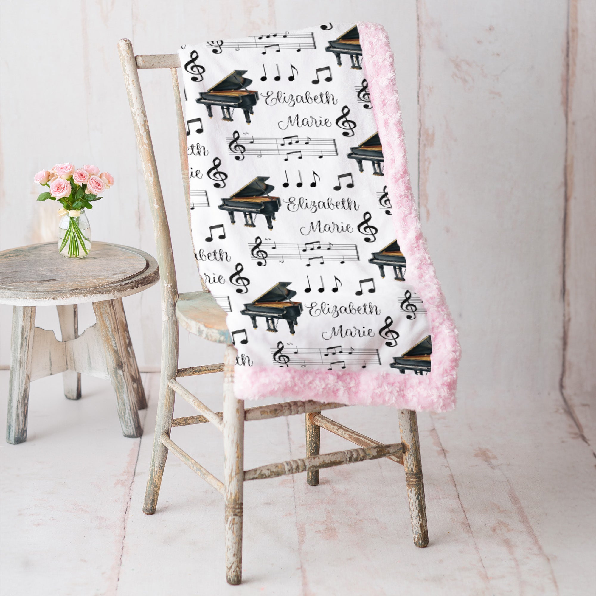 Personalized piano minky blanket with pink trim draped over vintage chair beside pink roses