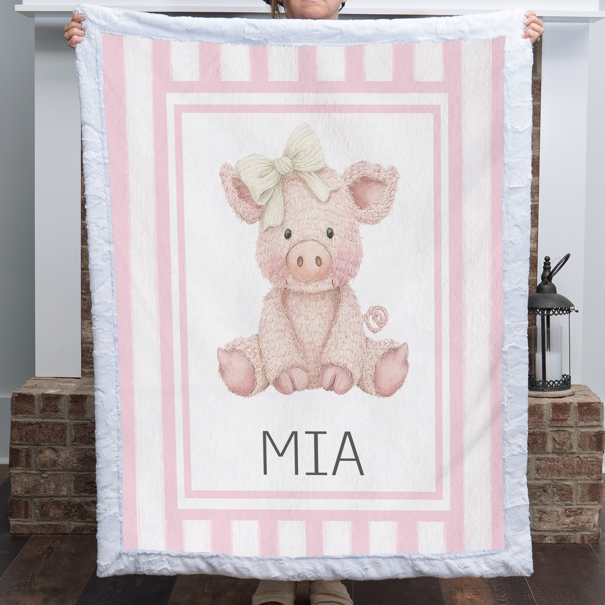 Personalized Luxe Cuddle Minky pig baby blanket with pink stripe border held up by fireplace
