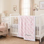 Personalized pink floral minky baby blanket draped over crib rail in nursery