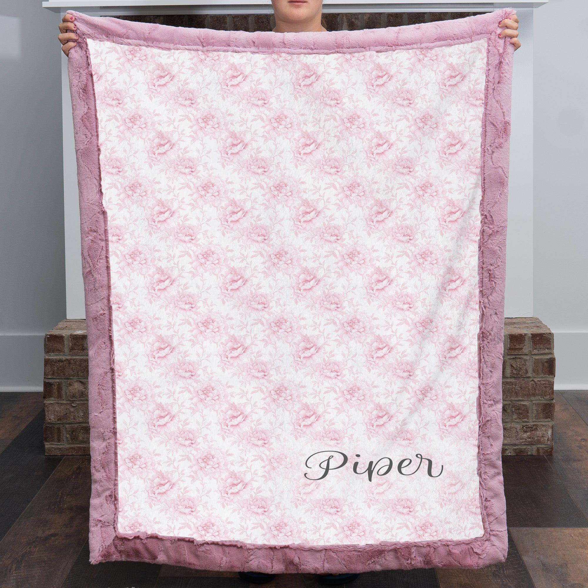 Personalized pink floral minky blanket with faux fur trim held up by fireplace mantel
