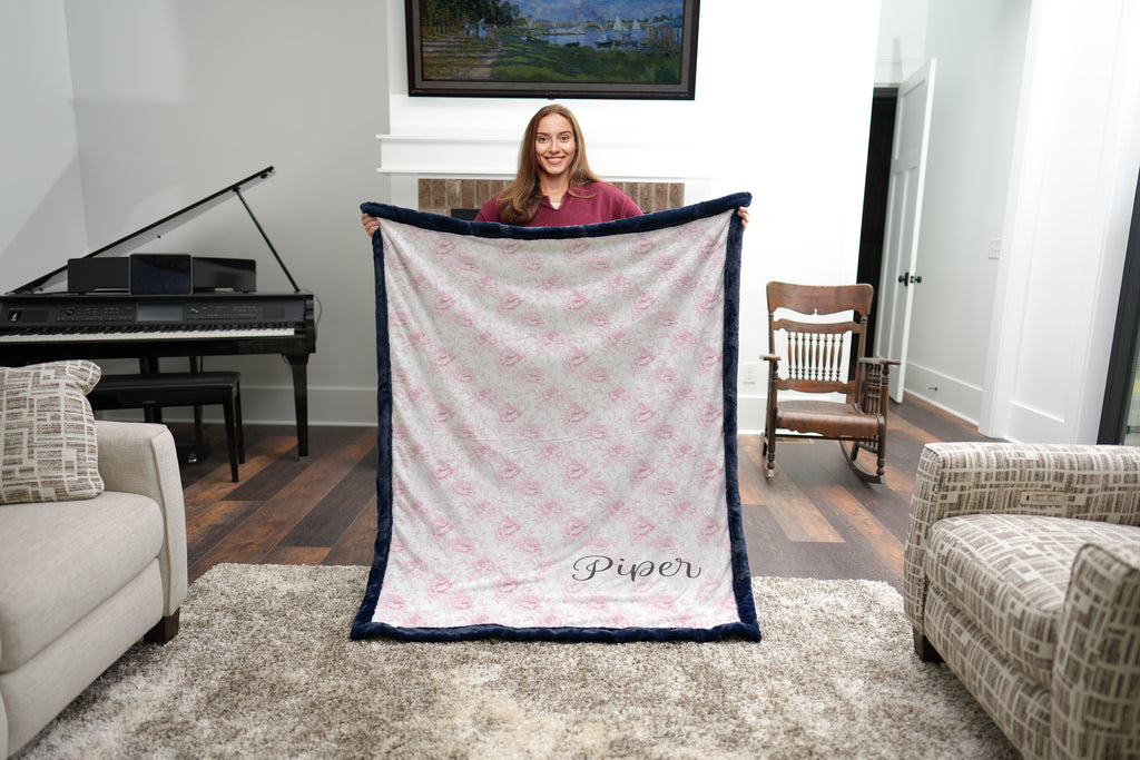Woman holding personalized pink floral minky blanket with navy faux fur trim in living room