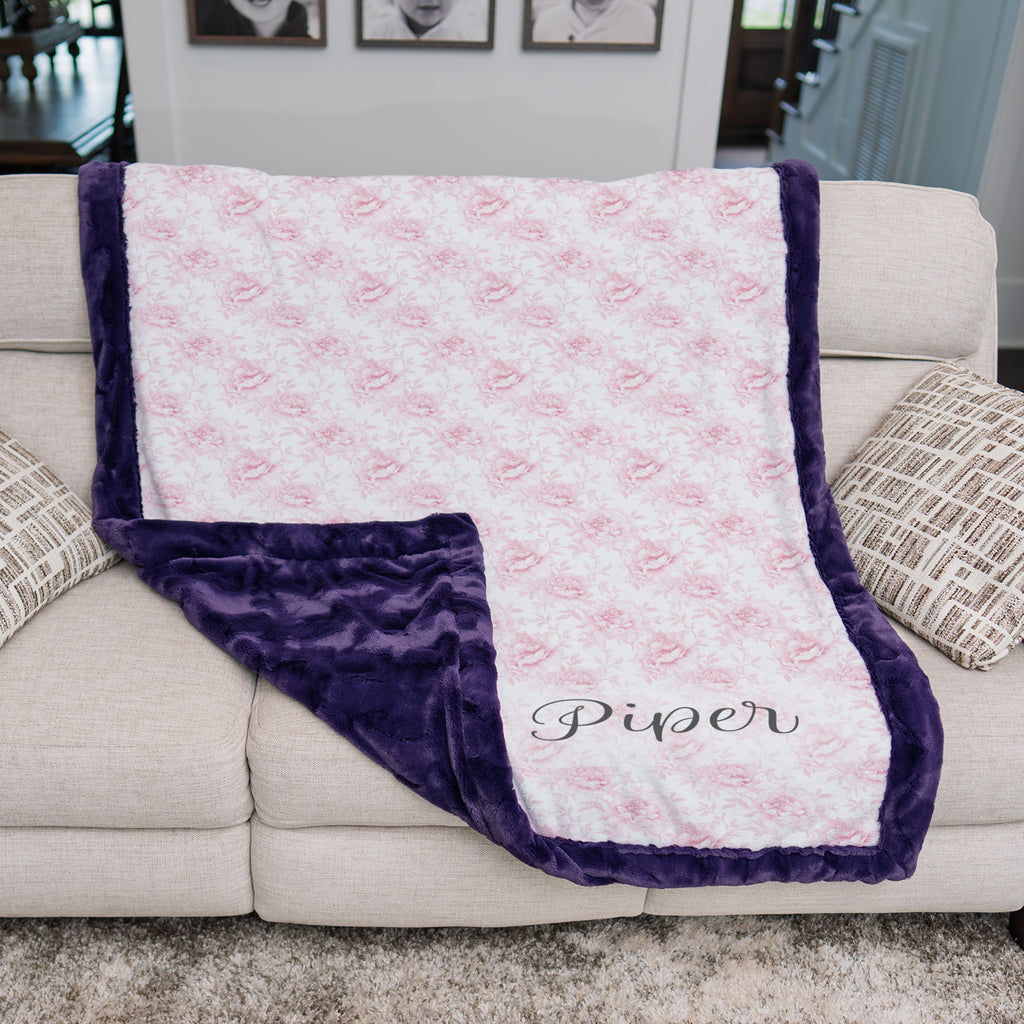 Personalized pink floral minky blanket with plum faux fur trim draped over couch