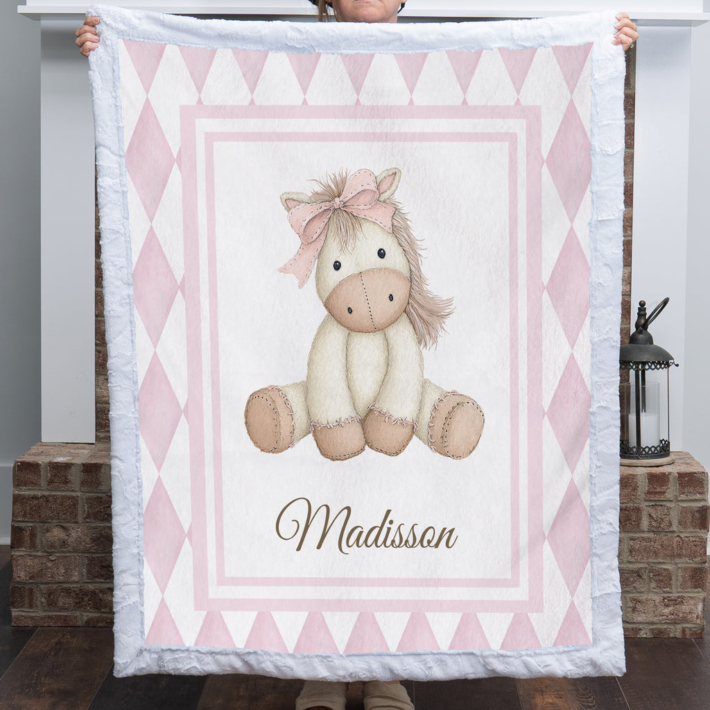 Personalized pink pony minky baby blanket with custom name, held up by fireplace mantel