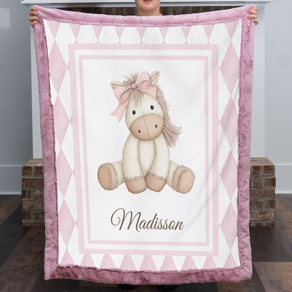 Personalized pink pony minky baby blanket with mauve fur trim, held up by fireplace