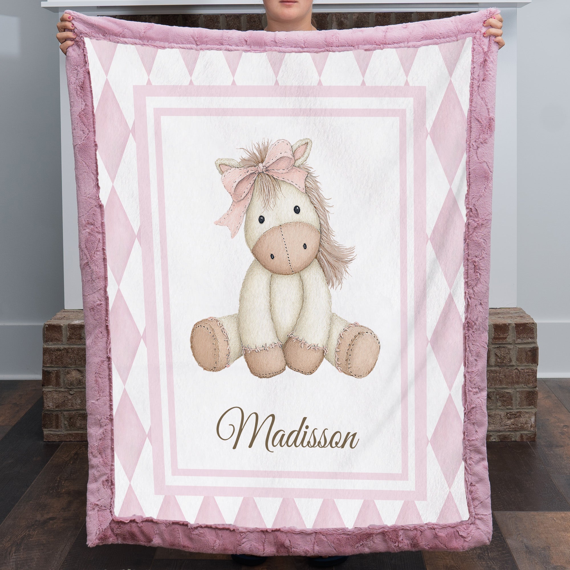 Personalized pink pony minky baby blanket with mauve fur trim, held up by fireplace