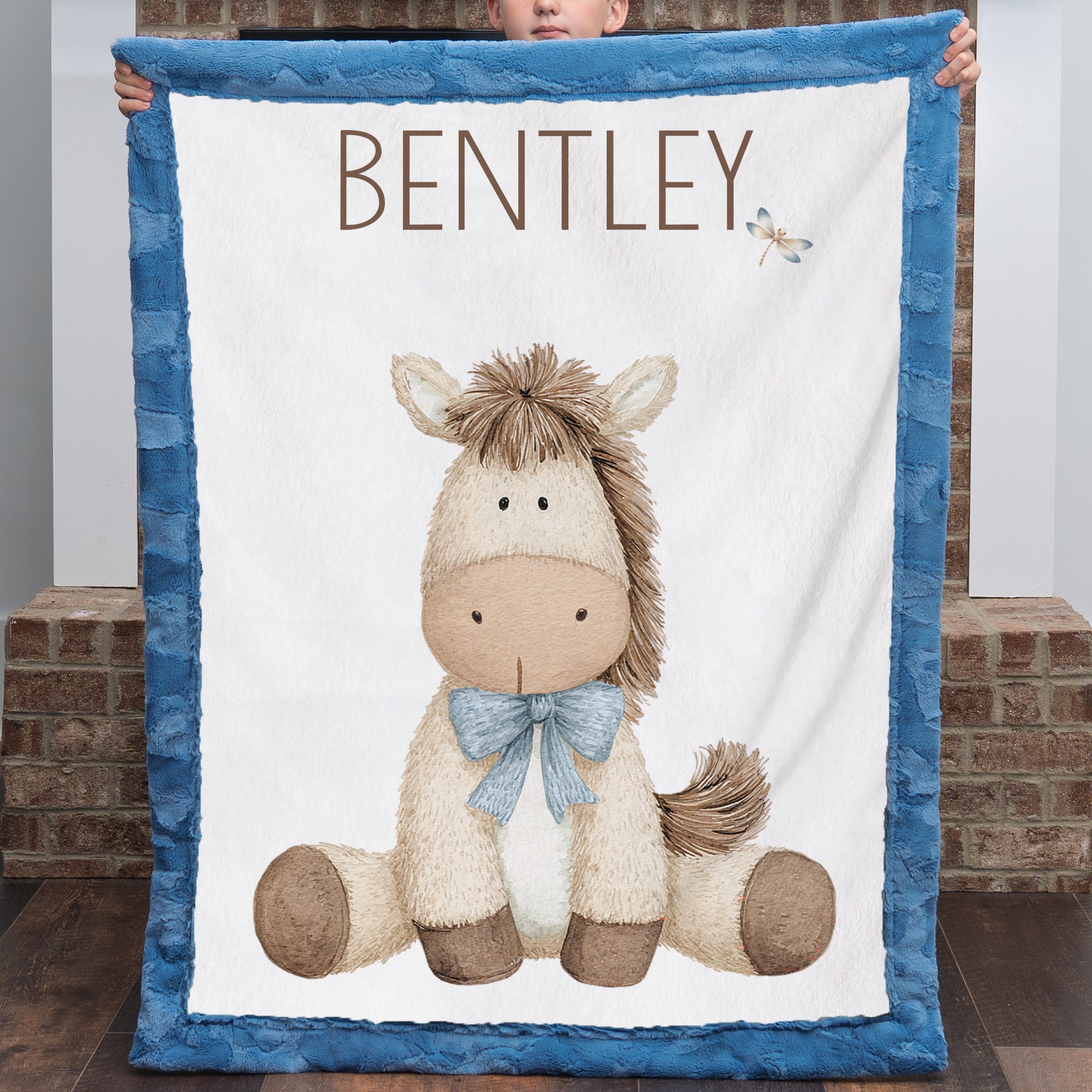 Boy holding personalized pony baby blanket with blue minky trim by brick fireplace