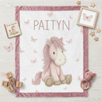 Personalized pony baby blanket with pink minky trim and butterflies, flat-laid with nursery props