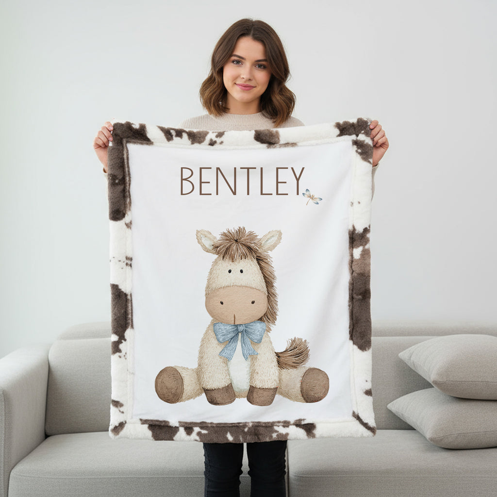 Woman holding personalized pony baby blanket with cow-print minky trim by fireplace mantel