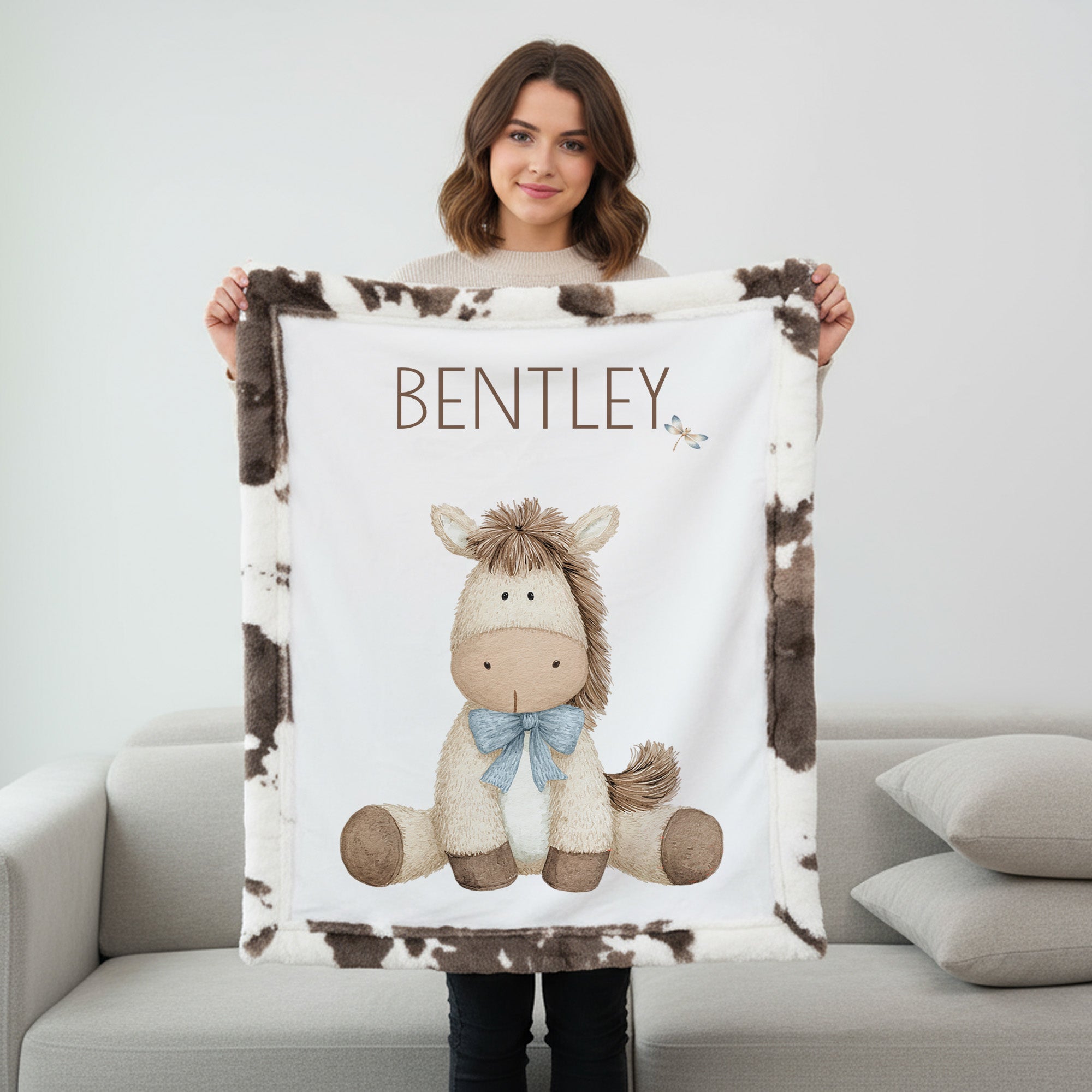 Woman holding personalized pony baby blanket with cow-print minky trim by fireplace mantel