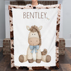 Woman holding personalized pony baby blanket with cow-print minky trim by fireplace