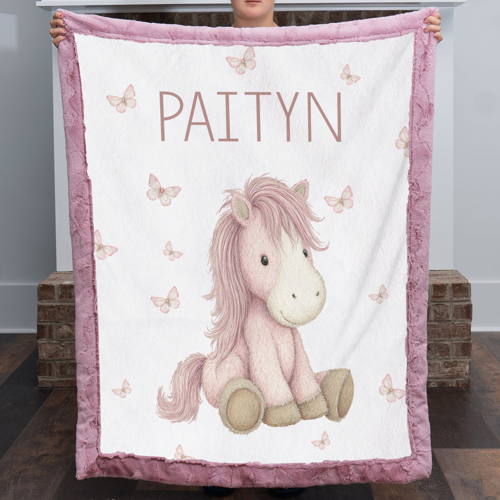 Woman holding personalized pony baby blanket with pink minky trim by fireplace mantel