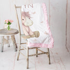 Personalized pony baby blanket with pink minky trim draped over vintage rustic chair