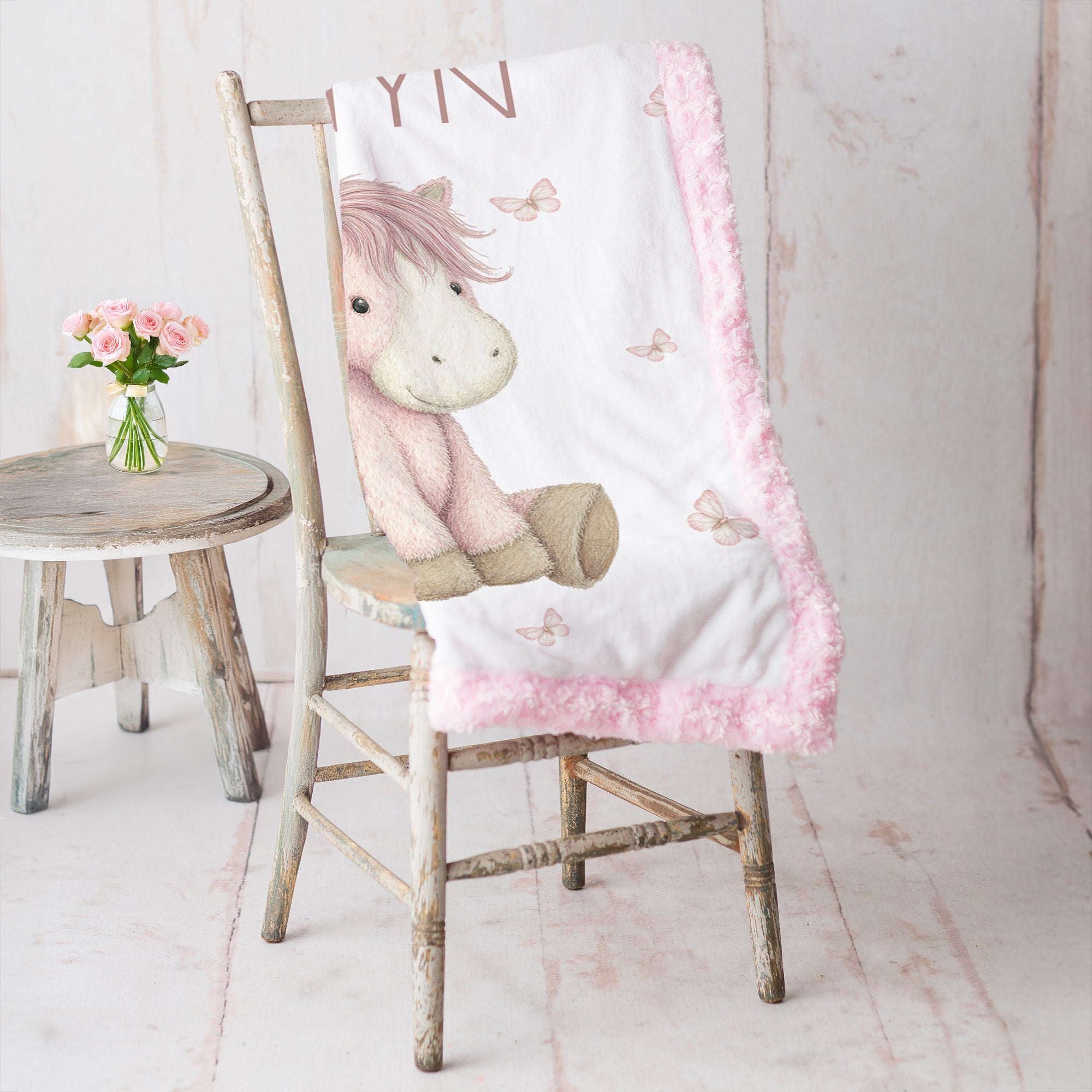 Personalized pony baby blanket with pink minky trim draped over vintage rustic chair