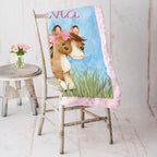 Personalized pony minky baby blanket with custom name draped on rustic white chair with pink roses