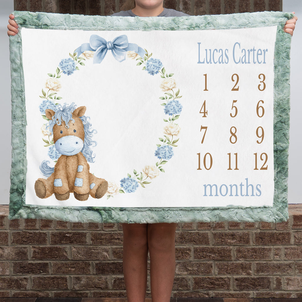 Personalized pony milestone minky blanket with sage trim held up outdoors
