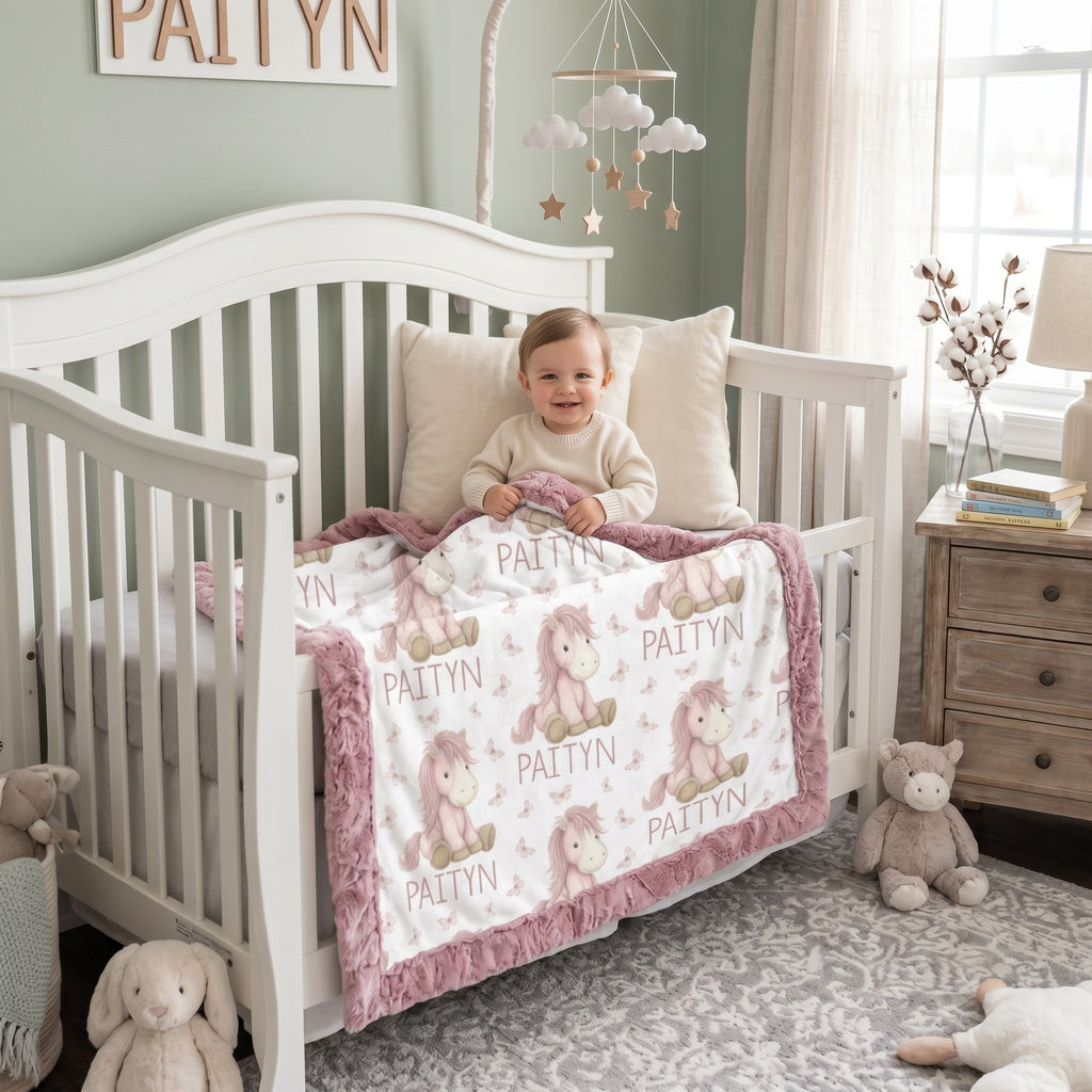 Toddler in crib holding personalized pony name blanket with mauve minky trim