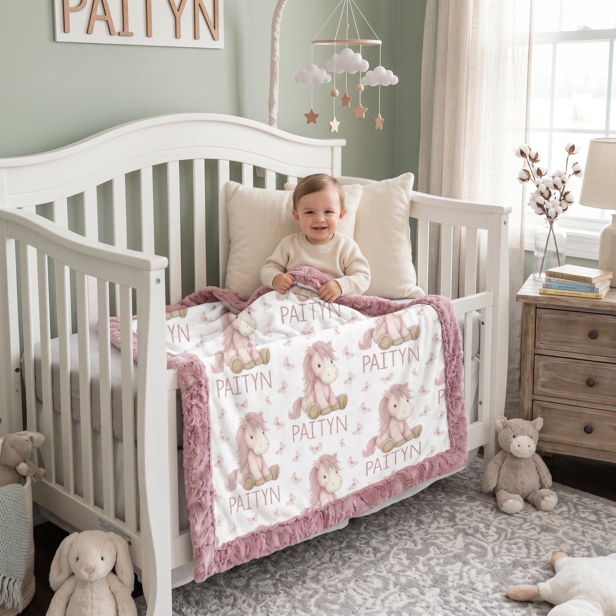 Toddler in crib holding personalized pony name blanket with mauve minky trim