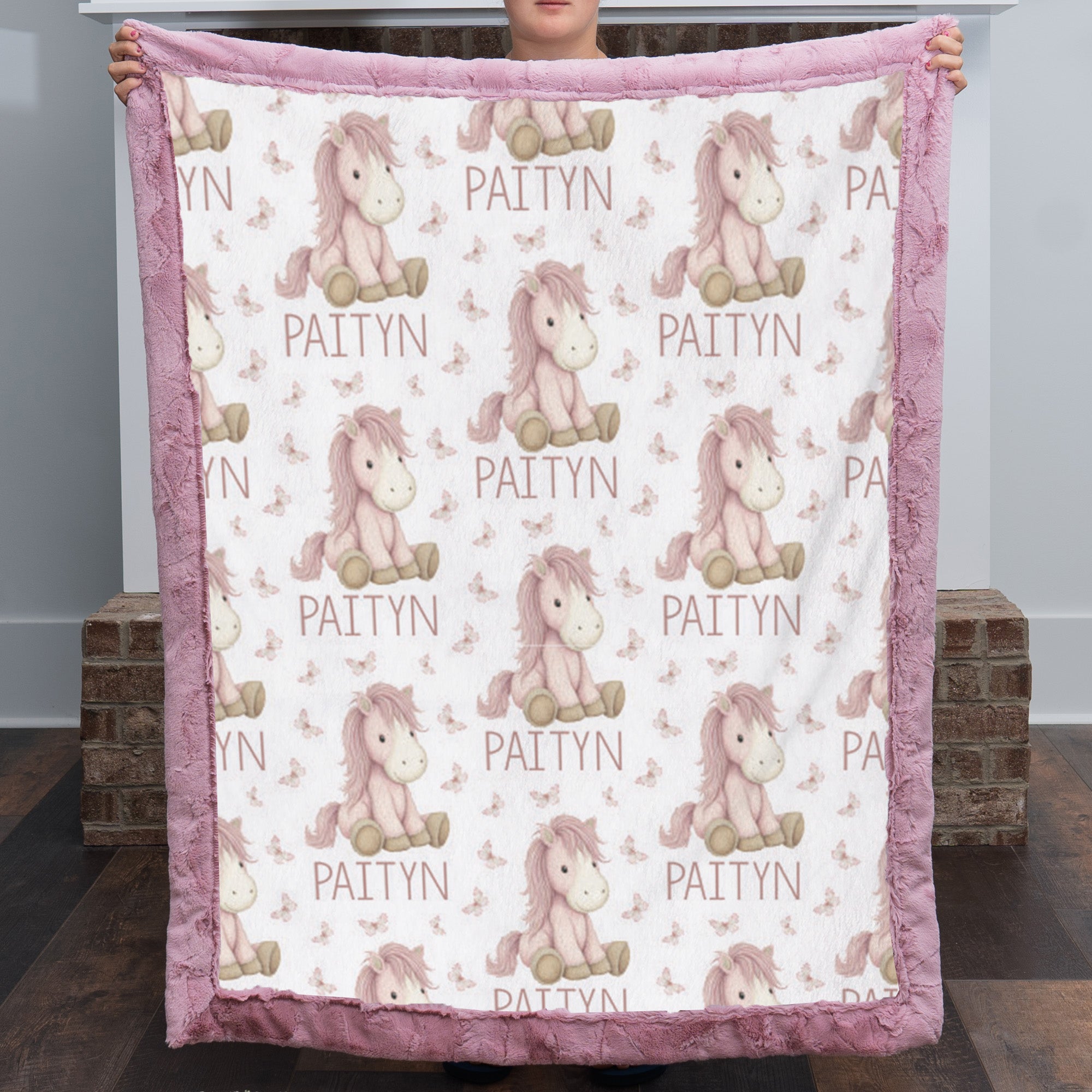 Woman holding personalized pony name blanket with pink minky trim by fireplace mantel