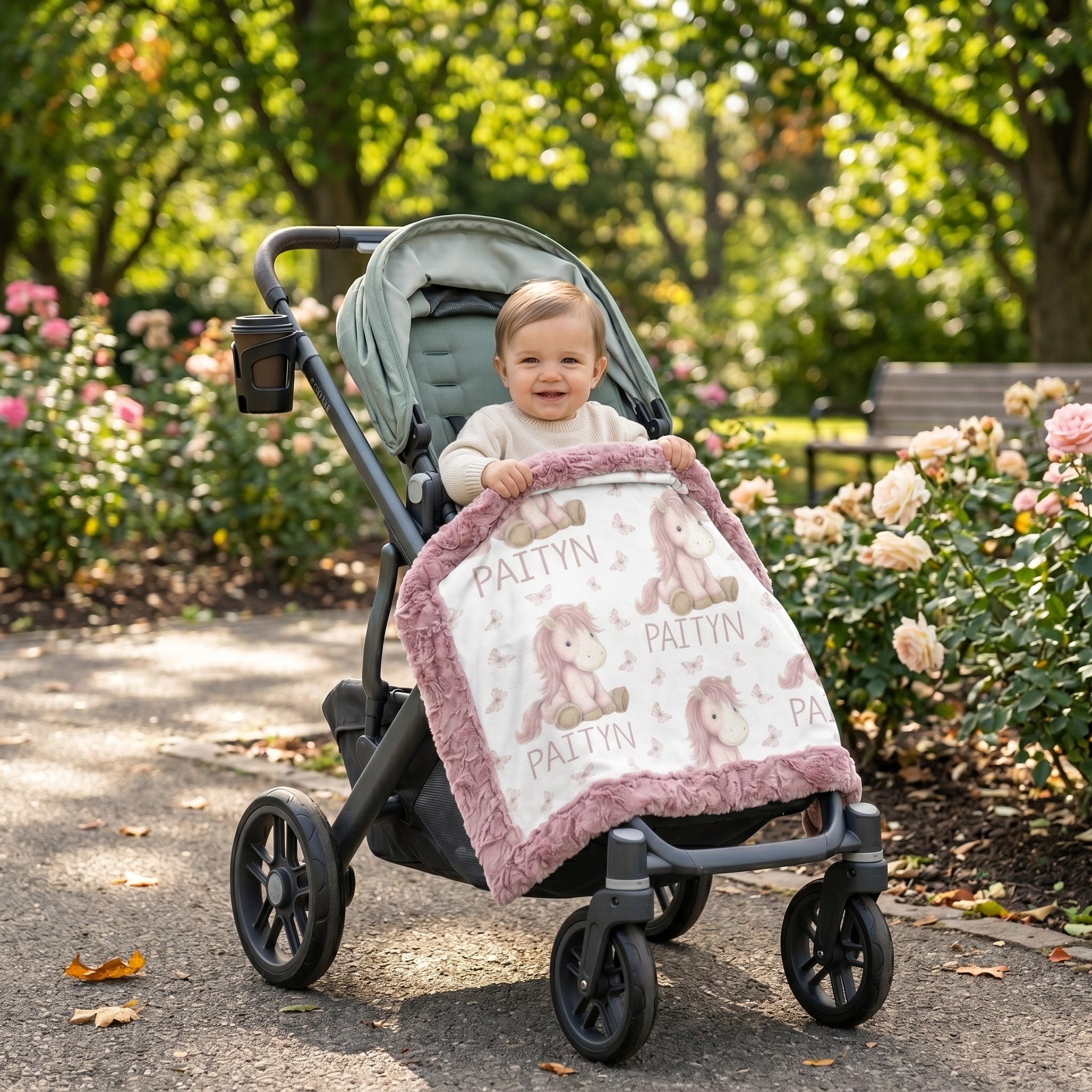 Toddler in stroller holding personalized pony name blanket with mauve minky trim in park