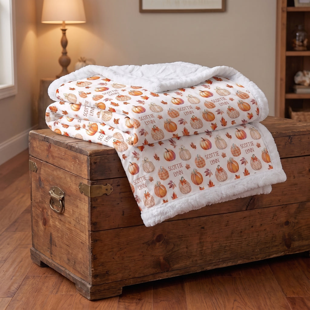 Folded personalized pumpkin patch minky blanket stacked on wooden trunk, white faux fur trim