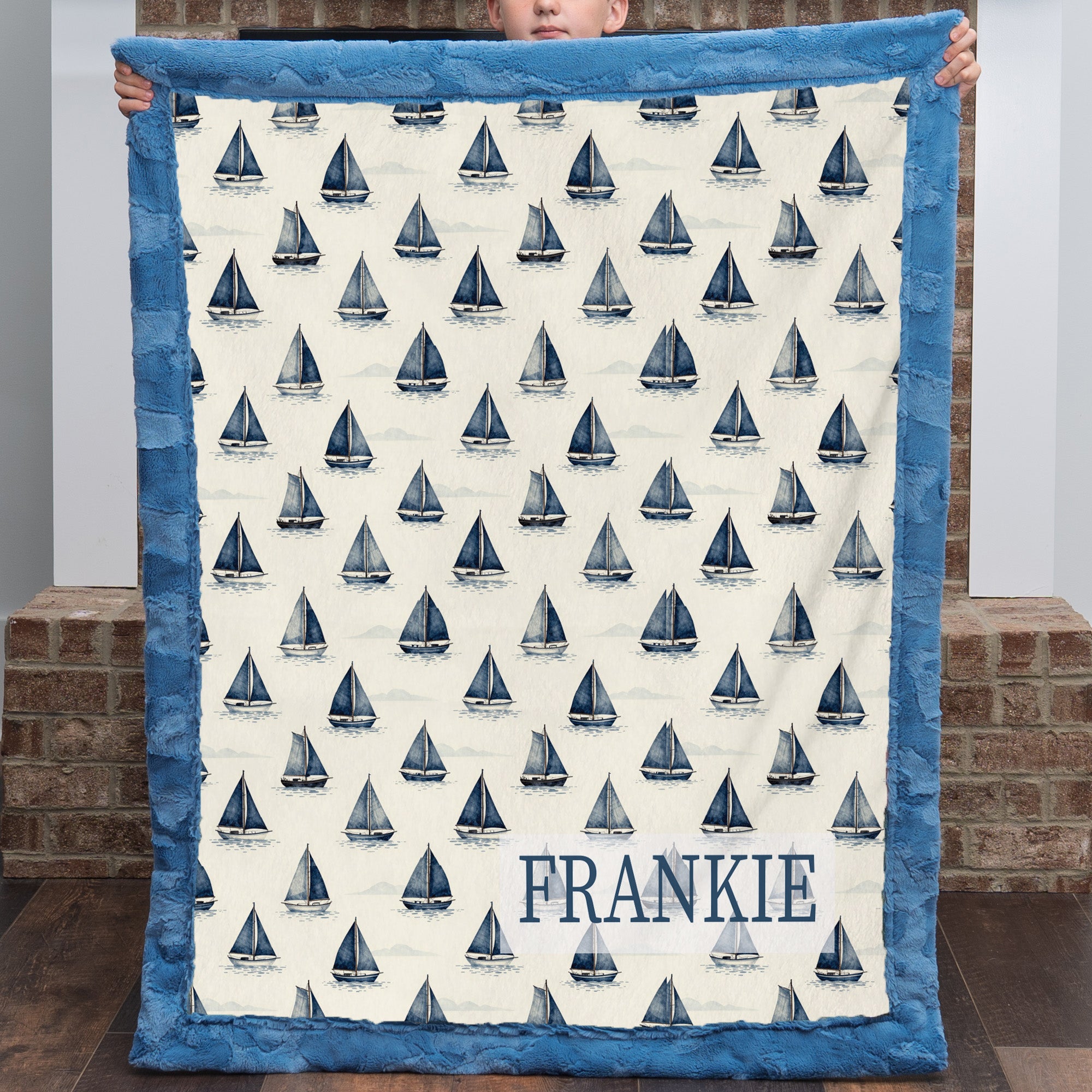 Personalized sailboat blanket with FRANKIE name, held up in front of brick fireplace