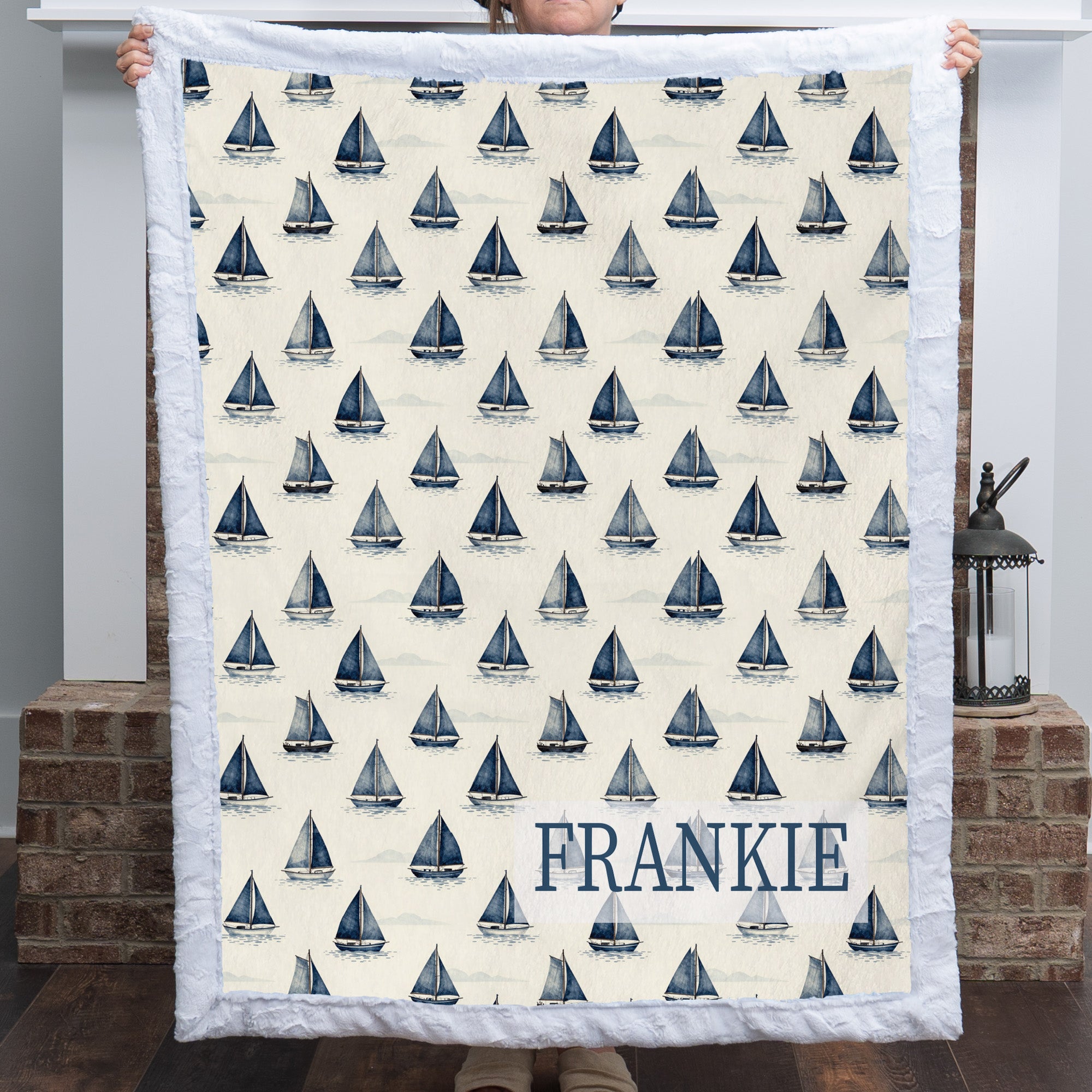 Personalized sailboat minky blanket with FRANKIE name held up by fireplace