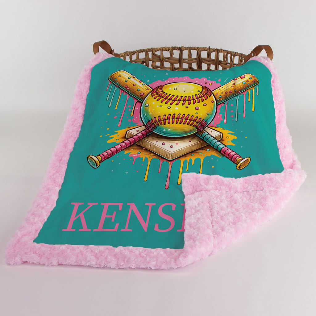 Personalized softball minky blanket draped over wicker basket with pink minky backing folded