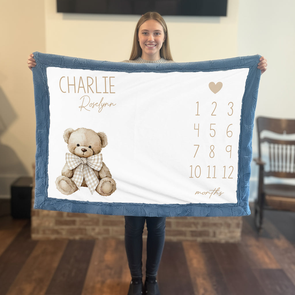 Woman holding personalized teddy bear milestone minky blanket with blue trim in living room