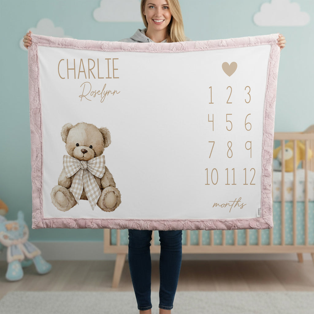 Woman holding personalized teddy bear milestone minky blanket with pink trim in cloud nursery